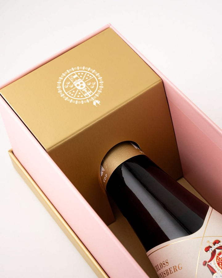 Weinflasche Schloss Johannisberg Riesling Goldlack 2020 in geöffneter pinker Geschenkbox, ornamentales Etikett mit Wappenschild; Außencover mit Kupferstich und Aufschrift The First Riesling Estate of the World
